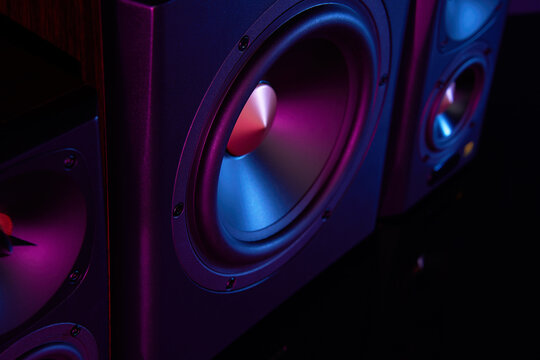 Two sound speakers and subwoofer on dark background with neon lights. Set for listening music. Acoustic equipment