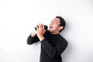 Portrait of carefree Asian man, having fun karaoke, singing in microphone while standing over white background