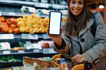 Close up of woman using app on mobile phone while buying in supermarket.