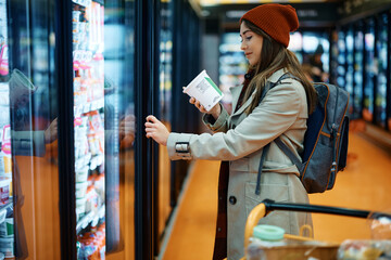 Young woman reads dairy product nutrition label while buying in supermarket.