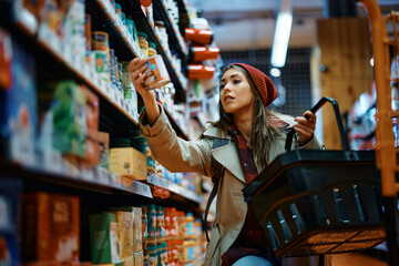 Young woman buying canned food at grocery store.