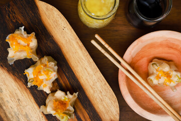 a hand tries to take dimsum from a wooden bowl using chopsticks