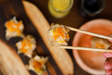 a hand tries to take dimsum from a wooden bowl using chopsticks