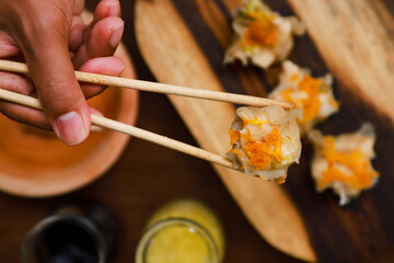 a hand tries to take dimsum from a wooden bowl using chopsticks