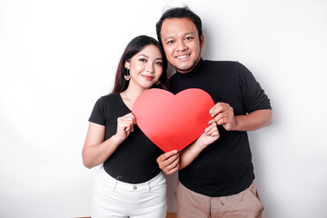 Fototapeta na wymiar A young Asian couple smiling and holding red heart-shaped paper, isolated by white background