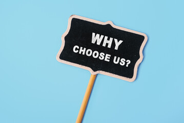 Why choose us - text on a small chalkboard on a blue background. Top view. Concept meaning list of advantages and disadvantages to select product or service
