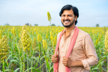 Portrait shot of happy young indian farmer standing with crossed arms by looking camera at farmland - concept of successful farming, and agricultural