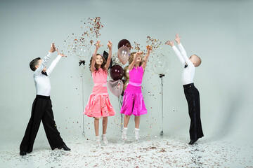 two curly-haired girls and two boys engaged in ballroom dancing, laughing and mischievously posing...