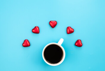 Chocolate sweets in the form of hearts and a cup of coffee on a blue background.