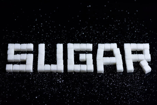 High angle shot of a sugar cubes on a black background. where you can read the message Sugar. selective focus.