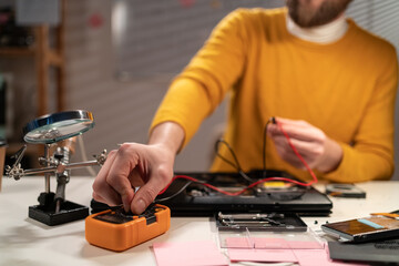 Concentrated technician busy repairing laptop at workshop using multimeter. Concept of skill jobs and repair service.