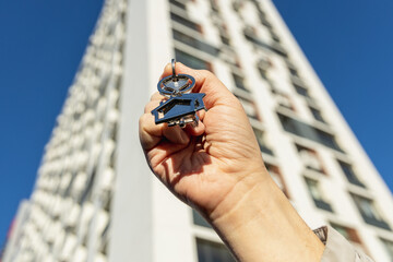 a man's hand holds the key to a new apartment on the background of a new building