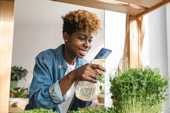 Smiling influencer spraying water on plants and vlogging over mobile phone at home