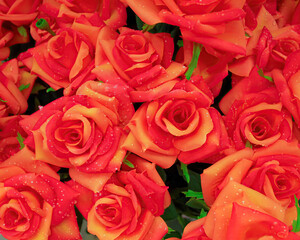 Dark orange artificial handmade roses with water drops bouquet, floral background.