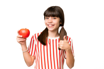 Little caucasian girl holding an apple over isolated background with thumbs up because something good has happened