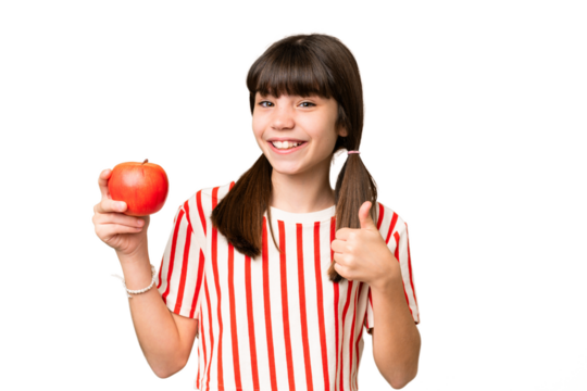 Little caucasian girl holding an apple over isolated background with thumbs up because something good has happened