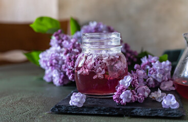 Preparation of syrup from the lilac flowers. Glass jar of homemade lilac syrup and branch of lilac flowers, stone background.
