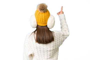 Little caucasian girl wearing winter muffs over isolated background pointing back with the index finger