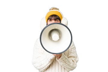 Little caucasian girl wearing winter muffs over isolated background shouting through a megaphone