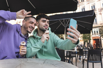 Happy gay couple with ice cream taking selfie through smart phone at cafe