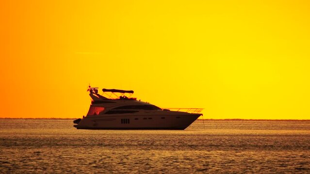 Luxury cruise trip. Red burning sunset over the sea with silhouette of yacht. Abstract nature summer ocean sea background. Small waves on golden warm water surface with bokeh lights from sun.