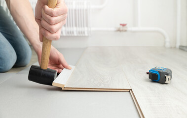 Man lays a laminate on the floor, hammering it with a rubber mallet. Repair and decoration of...