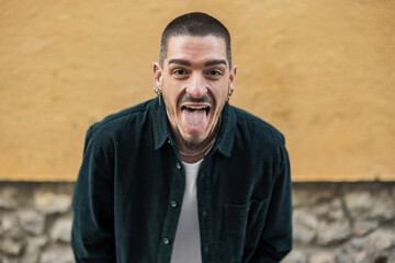 Happy man sticking out tongue in front of wall