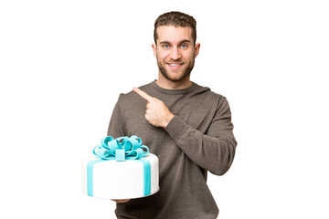 Young handsome blonde man holding birthday cake over isolated chroma key background pointing to the side to present a product