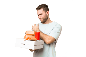 Young handsome blonde man holding pizzas and burgers over isolated background suffering from pain in shoulder for having made an effort