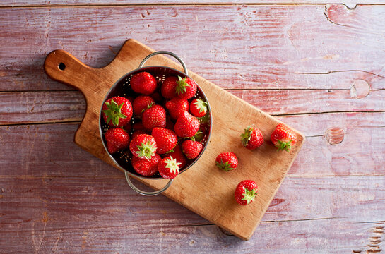 Colander with fresh strawberries lying on cutting board