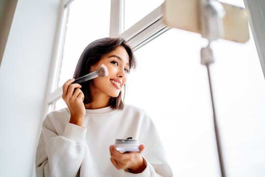 Young influencer applying blusher and filming through mobile phone at home