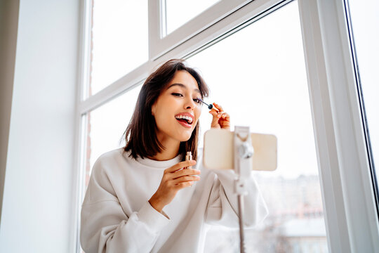 Happy influencer filming make-up tutorial through smart phone