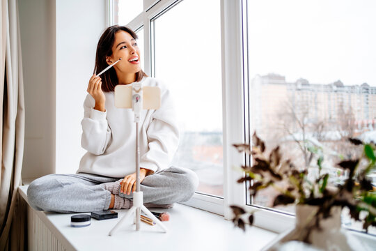 Happy influencer doing make-up and filming through smart phone