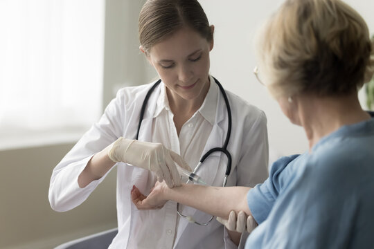 Focused Medical Nurse Giving Shot To Vein Of Older Patient, Vaccinating Lady Against Covid, Flu. Senior Woman Getting Injection For Immunity Protection From Respiratory Infection Disease