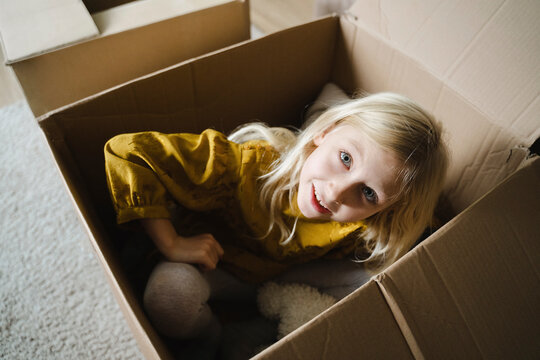 Girl sitting inside cardboard box at home