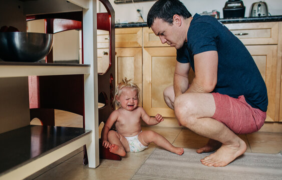 Dad looks down at diapered toddler girl while crying in kitchen