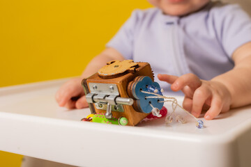 a cute kid is sitting in a child's chair playing with an educational wooden toy on a yellow background. bizi-board