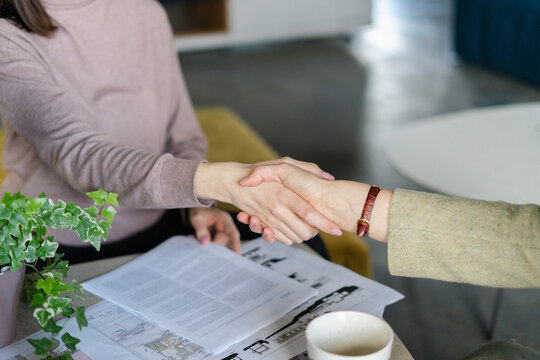 Two women shaking hands above construction plan on table