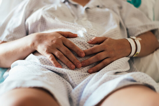 Young woman hospitalized in a bed. Gesture of pain in her belly.