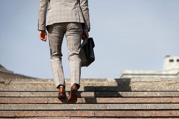 Man in a business suit with leather briefcase climbing stone stairs in city, male legs in motion on the steps. Concept of career, success, moving to the top, official or businessman