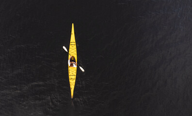 Aerial view of woman paddling yellow kayak on dark lake water.