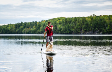Man paddling a stand up paddleboard SUP with his dog on a lake.