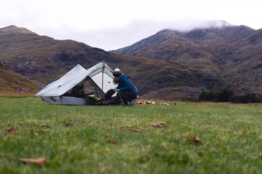 Female Camper setting up tent at foot of mountain