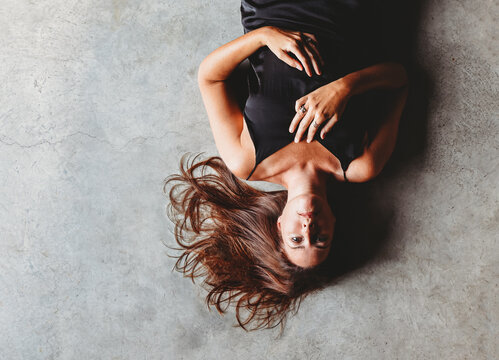 Overhead view of beautiful brunette woman laying on concrete floor.
