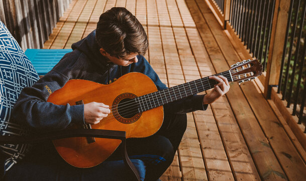 Teen boy playing an acoustic guitar on the deck of a log home. - Powered by Adobe