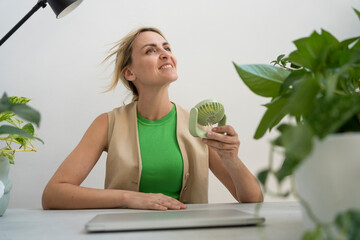 Happy freelancer with handheld motorized fan sitting at desk