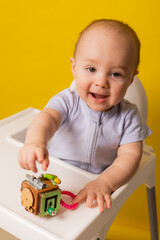 a cute kid is sitting in a child's chair playing with an educational wooden toy on a yellow background. bizi-board