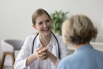 Cheerful GP doctor talking to mature patient woman, giving consultation, medical advice, smiling, laughing, telling examination good result. Happy female physician working in hospital office
