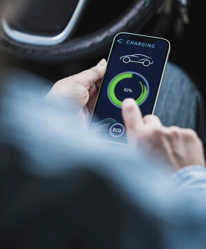 Hands of mature woman using mobile app to operate electric car