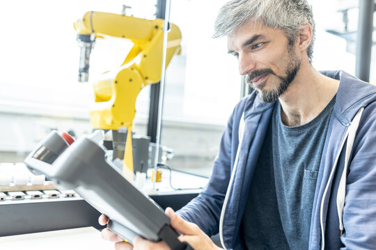 Skilled worker in robotic factory controlling robot arm with digital control